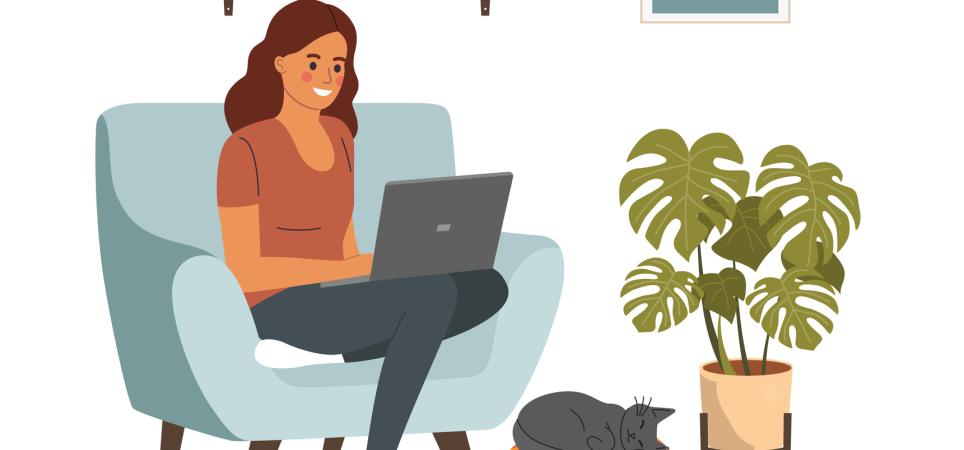 Woman sitting on her comfy chair at home, working on her laptop with her cat cozied up at her feet