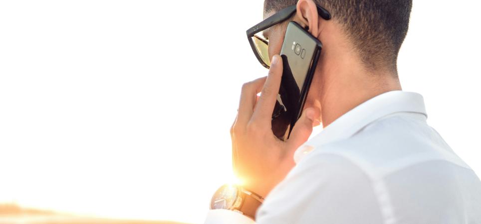 man speaking on the phone as the sun rises behind him